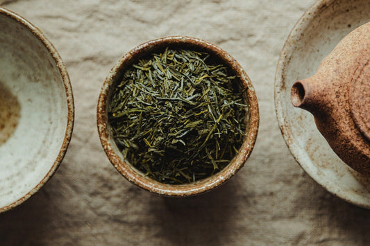 Cup of green tea next to a saucer and teapot