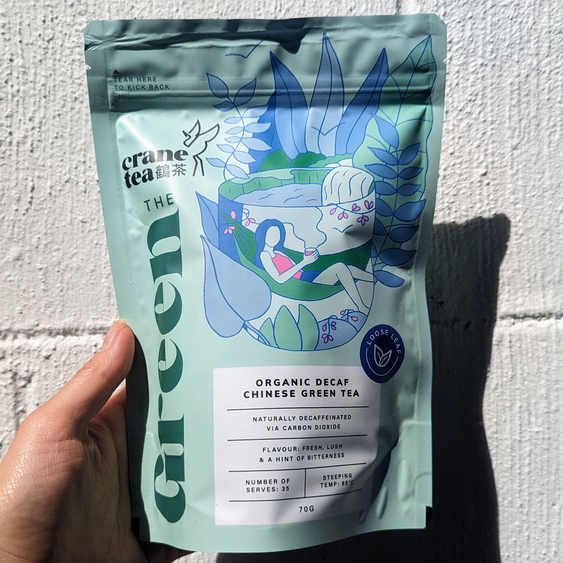 A hand holding a packet of Crane Tea Decaf Green